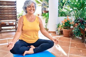 Middle age woman with grey hair smiling happy doing yoga on the terrace at home.