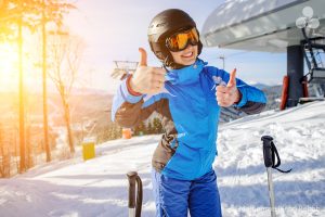 Young female skier at ski resort smiling and showing thumbs up.