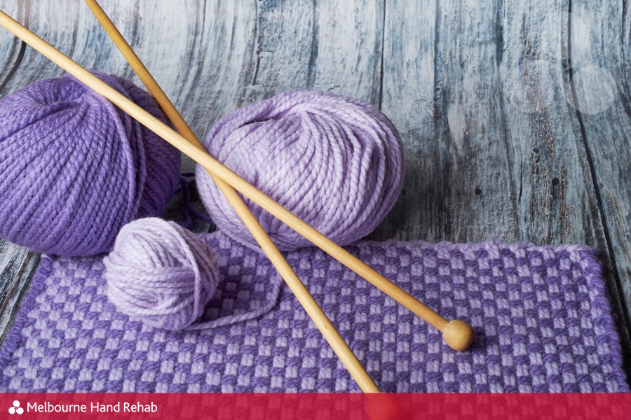 Image of wooden knitting needles, purple wool of various shades and sample of knitting on a grey faux timber background. Read our blog. Healing stitches: The therapeutic benefits of knitting and crocheting.
