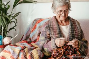 Image of elderly smiling woman knitting. Read our blog. Healing stitches: The therapeutic benefits of knitting and crocheting.